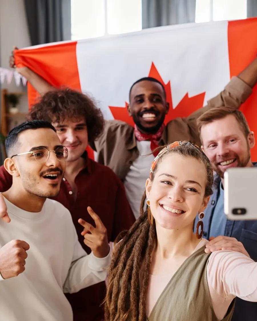 African man raising a Canadian flag during a group selfie with friends